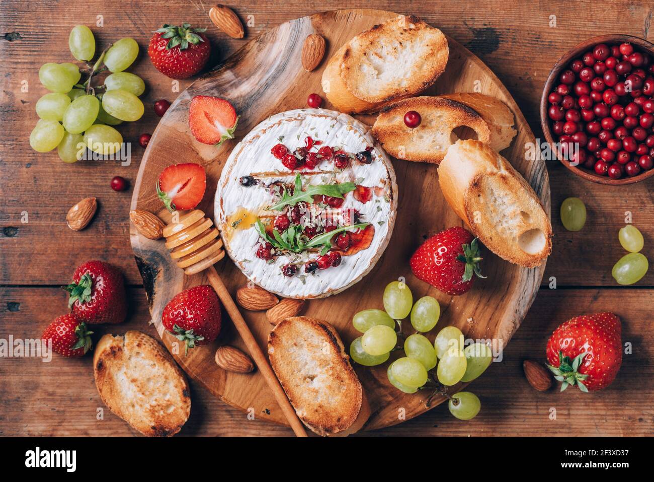 Formaggio camembert al forno con miele, rucola, mirtillo, pane tostato, uva, fragole, mandorle su tavola di legno. Vista dall'alto. Spazio di copia. Romantico Foto Stock