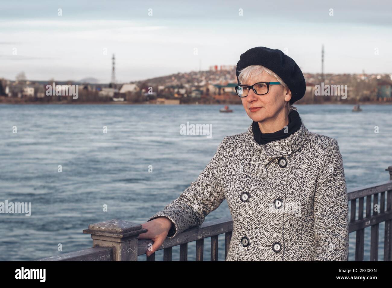 Ritratto di un'elegante donna di mezza età in occhiali sull'argine del fiume. Primo piano. Uno sguardo penoso sulla distanza. Solitudine, riflessione, Foto Stock