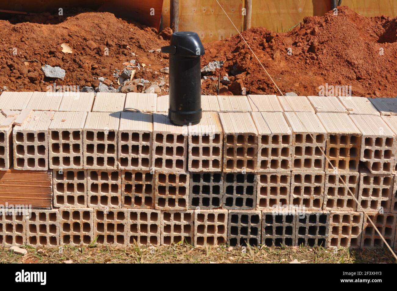Pila di blocchi di calcestruzzo con bottiglia termomica di caffè nero sulla parte superiore di terra rossa sfondo e di legno sul cantiere in Brasile, Sud am Foto Stock