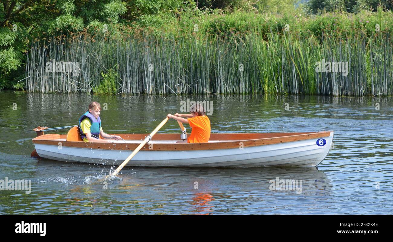Bambini in barca a remi sul fiume con canne e alberi sullo sfondo. Foto Stock