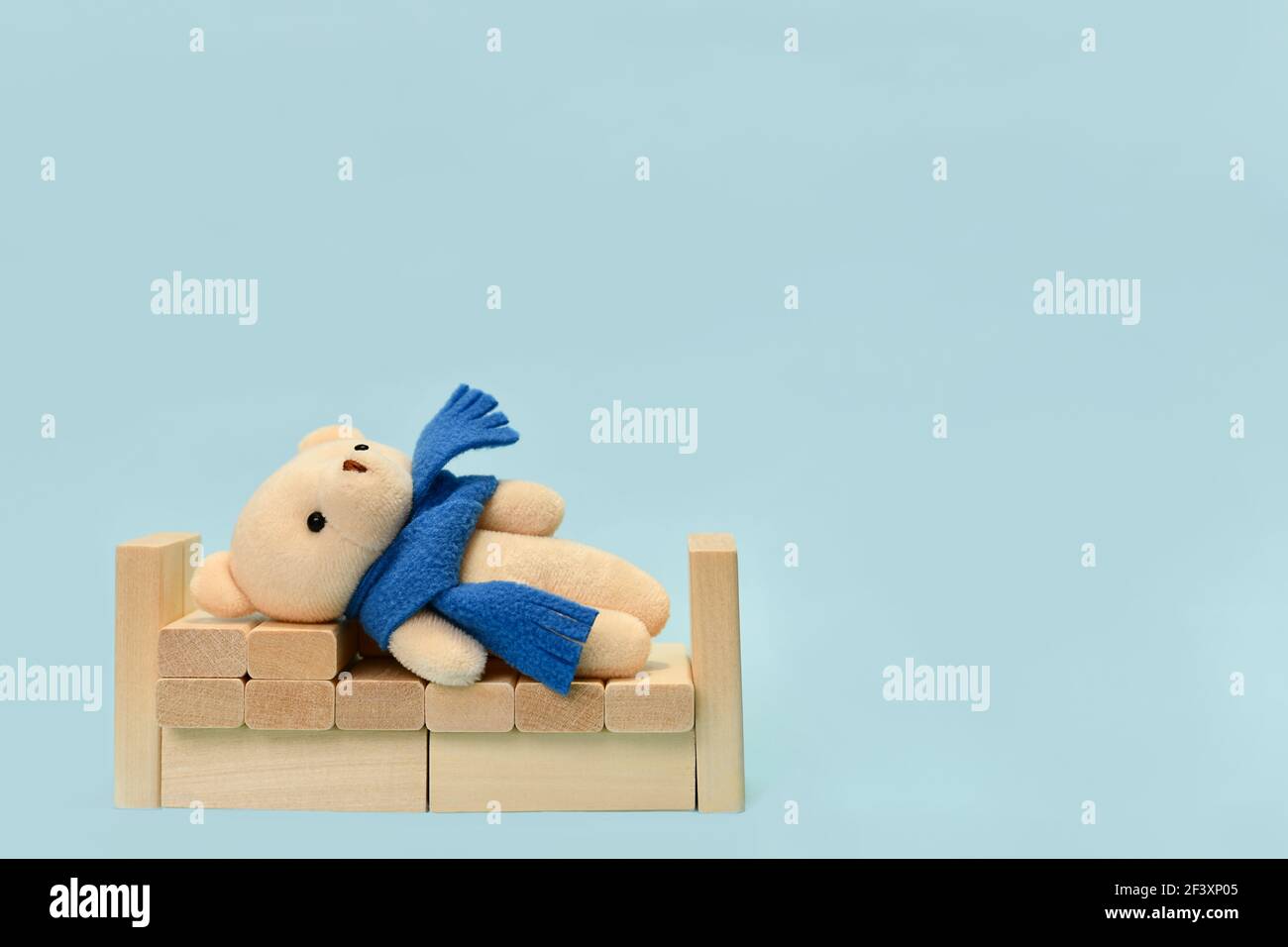 Un orsetto peluche giace in un presepe fatto di cubetti di legno. Su sfondo azzurro. Foto Stock