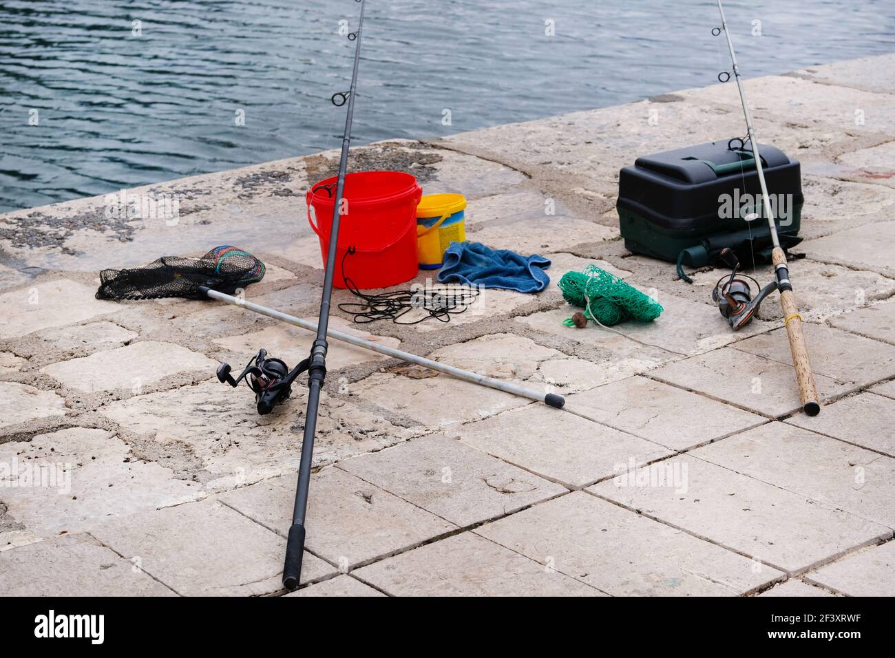 Attrezzatura da pesca sul molo di cemento sul mare. Pesca con canne e box. Foto Stock