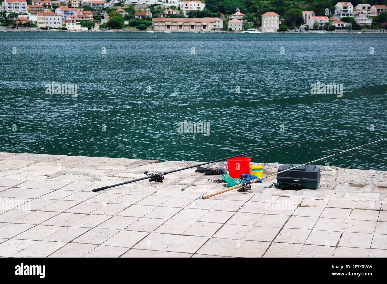 Attrezzatura da pesca sul molo di cemento sul mare. Immagine di due canne da pesca commerciali su acque turchesi. Foto Stock