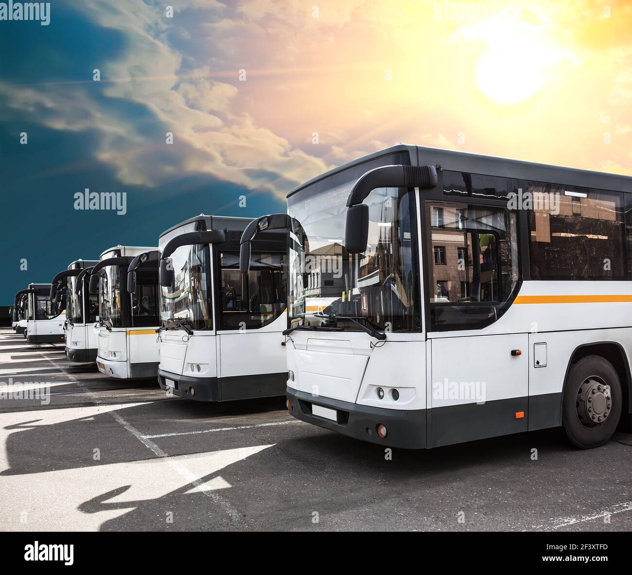 autobus urbani in fila in un parcheggio sotto un cielo soleggiato e nuvoloso Foto Stock