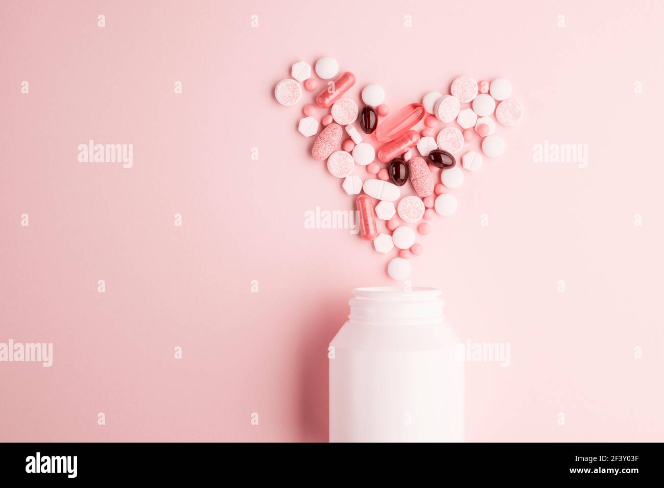 Pillole di medicina forma del cuore con bottiglia su sfondo rosa Foto Stock