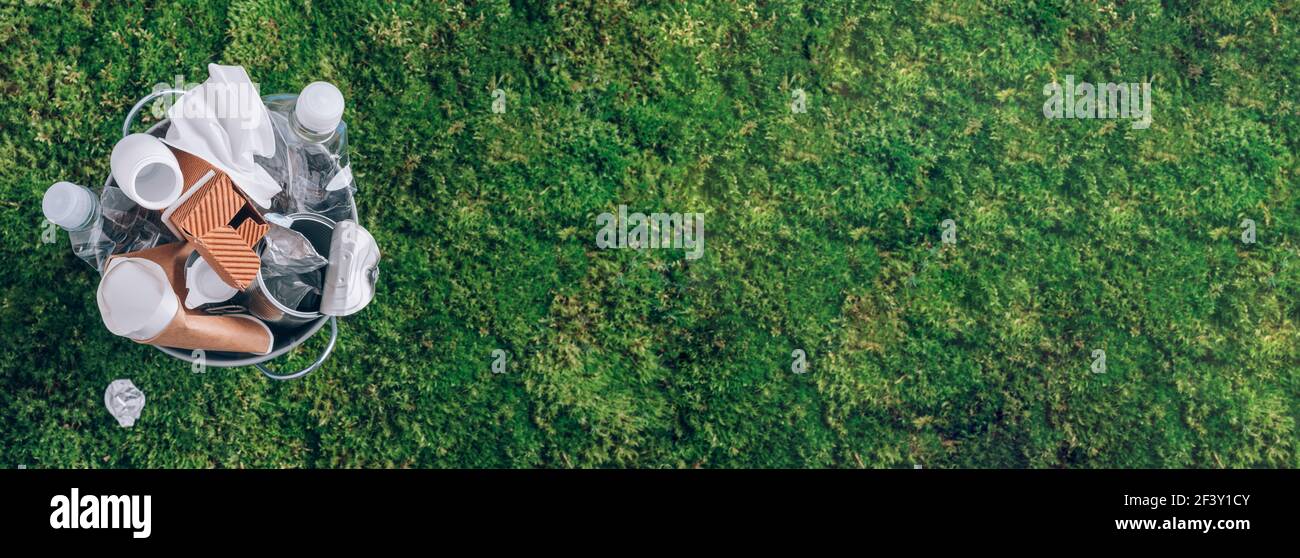 Riutilizzare rifiuti, riciclare, senza plastica. Banner. Confezione di plastica alimentare in cestino, sfondo muschio verde dopo pic-nic in foresta. Vista dall'alto. Riciclaggio Foto Stock