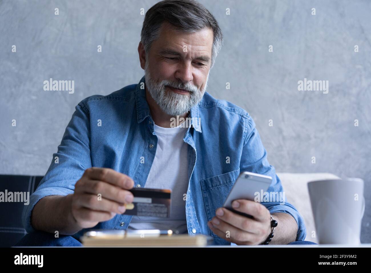 Sorridente uomo anni '50 con capelli grigi paga le bollette online  utilizzando uno smartphone moderno gadget e carta di credito Foto stock -  Alamy