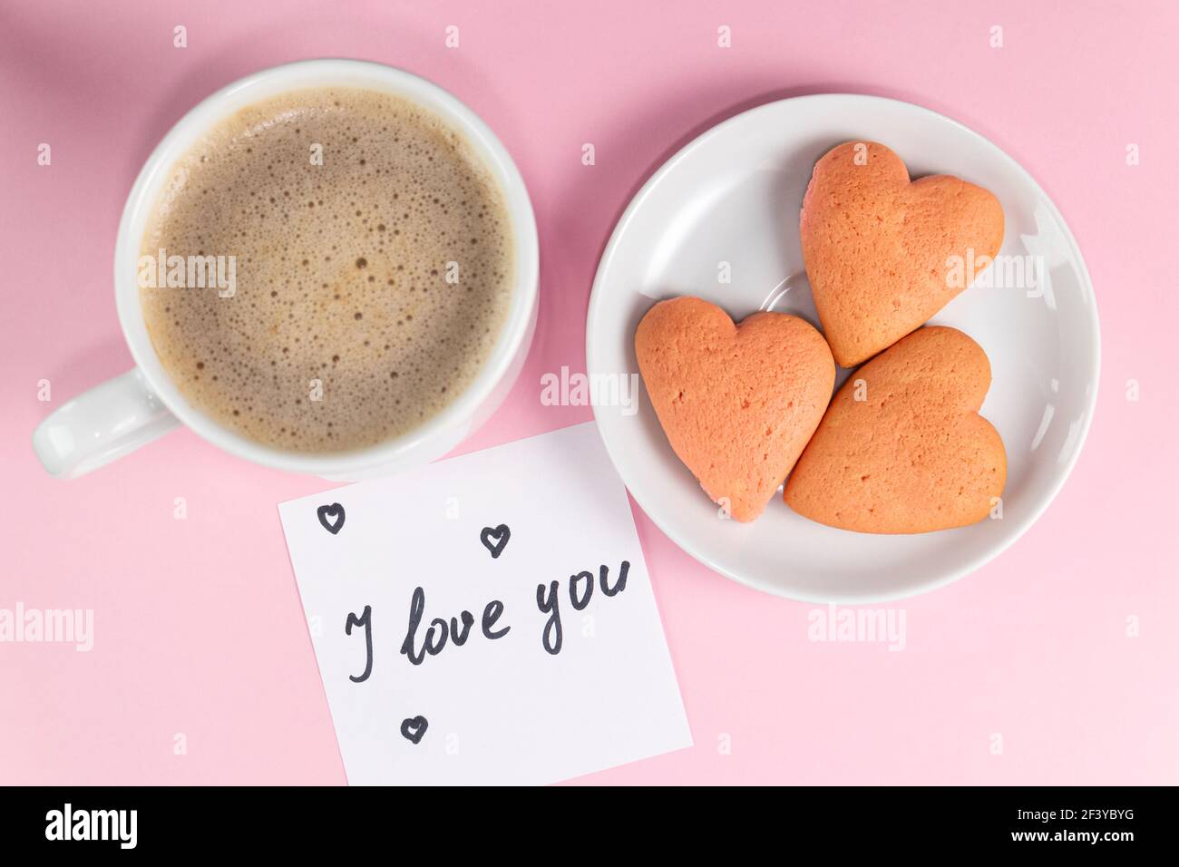 Nota con le parole ti amo con biscotti a forma di cuore e tazza di caffè di colore giallo pastello. Buona mattina o colazione di San Valentino Foto Stock
