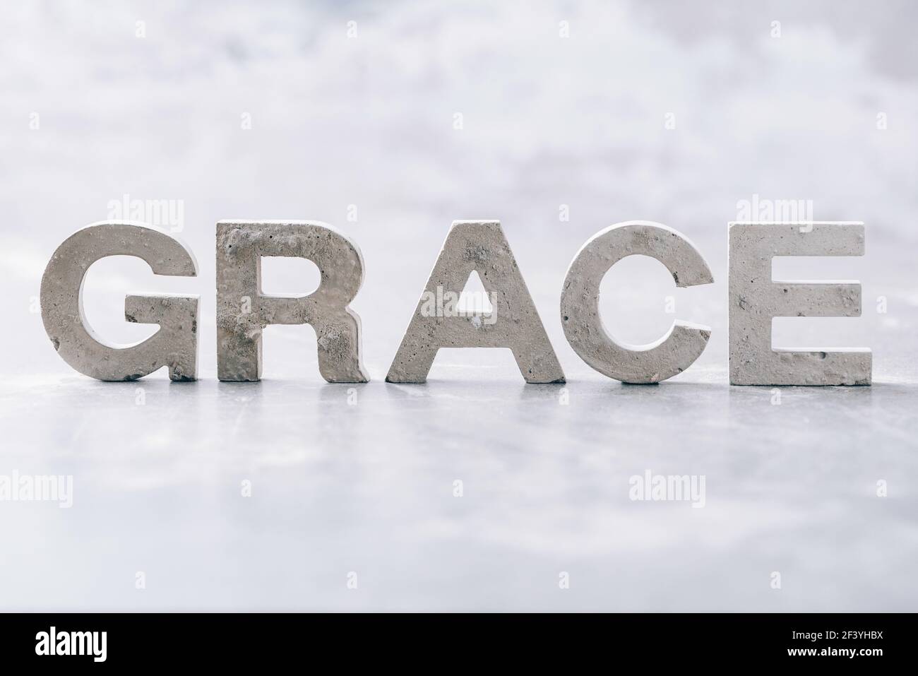Parola GRAZIA fatta con lettere di cemento su sfondo di marmo grigio. Spazio di copia. Promemoria biblico, spirituale o cristiano Foto Stock