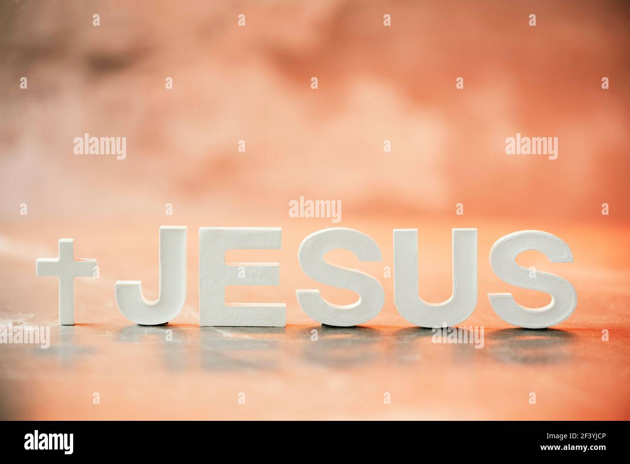 Nome GESÙ fatto con lettere di cemento su sfondo arancione chiaro marmo. Spazio di copia. Promemoria biblico, spirituale o cristiano Foto Stock