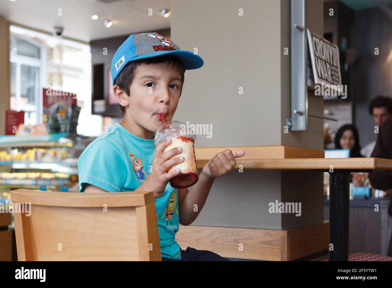 Young boy, 5-6 anni, beve frullato di latte di fragola in un bar, Londra, Inghilterra Foto Stock