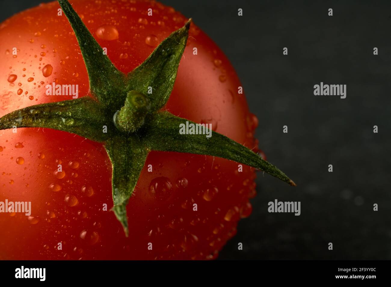 Singolo pomodoro rosso ciliegia su una tavola di pietra nera con fondo di legno. Può essere usato anche come sfondo o texture. Foto Stock