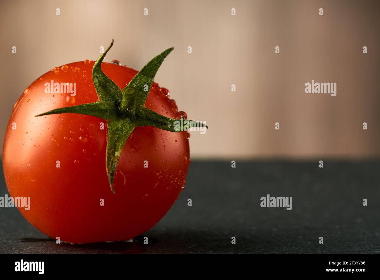 Singolo pomodoro rosso ciliegia su una tavola di pietra nera con fondo di legno. Può essere usato anche come sfondo o texture. Foto Stock