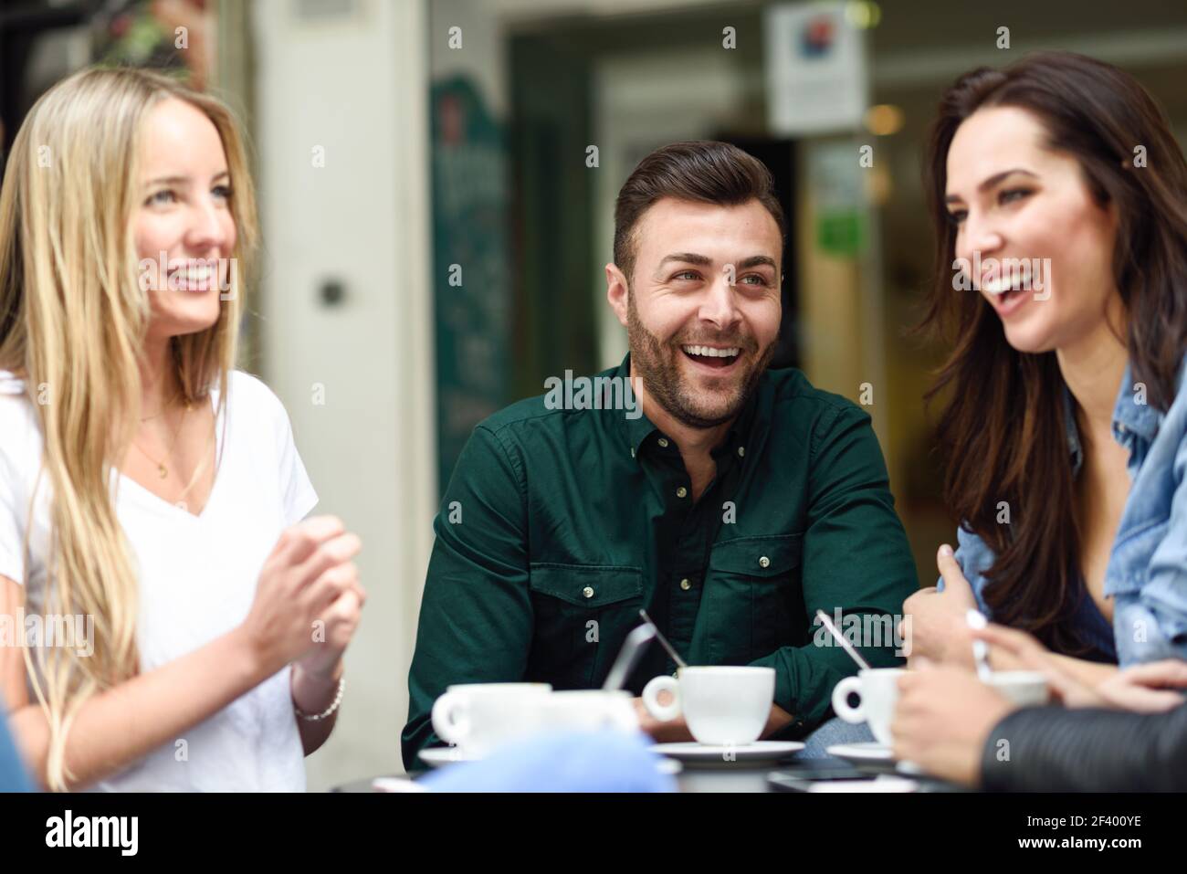 Gruppo multirazziale di amici che hanno un caffè insieme. Due donne e un uomo al caffè, parlando, ridendo e godendo il loro tempo. Stili di vita e concetti di amicizia con modelli di persone reali Foto Stock