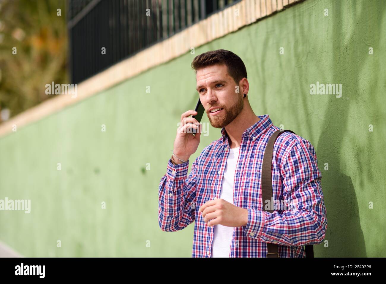 Giovane uomo che parla con il suo smart phone in background urbano. Ragazzo indossa abiti casual. Il concetto di stile di vita. Foto Stock