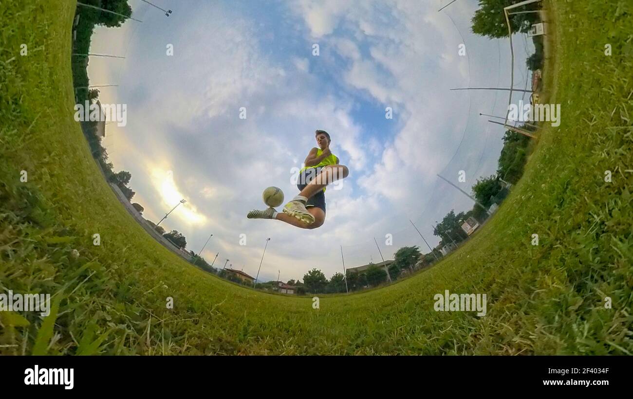 Caucasico ragazzo che gioca a calcio in campo. Stagione estiva, luce diurna, vista angolare, obiettivo fisheye. Foto Stock