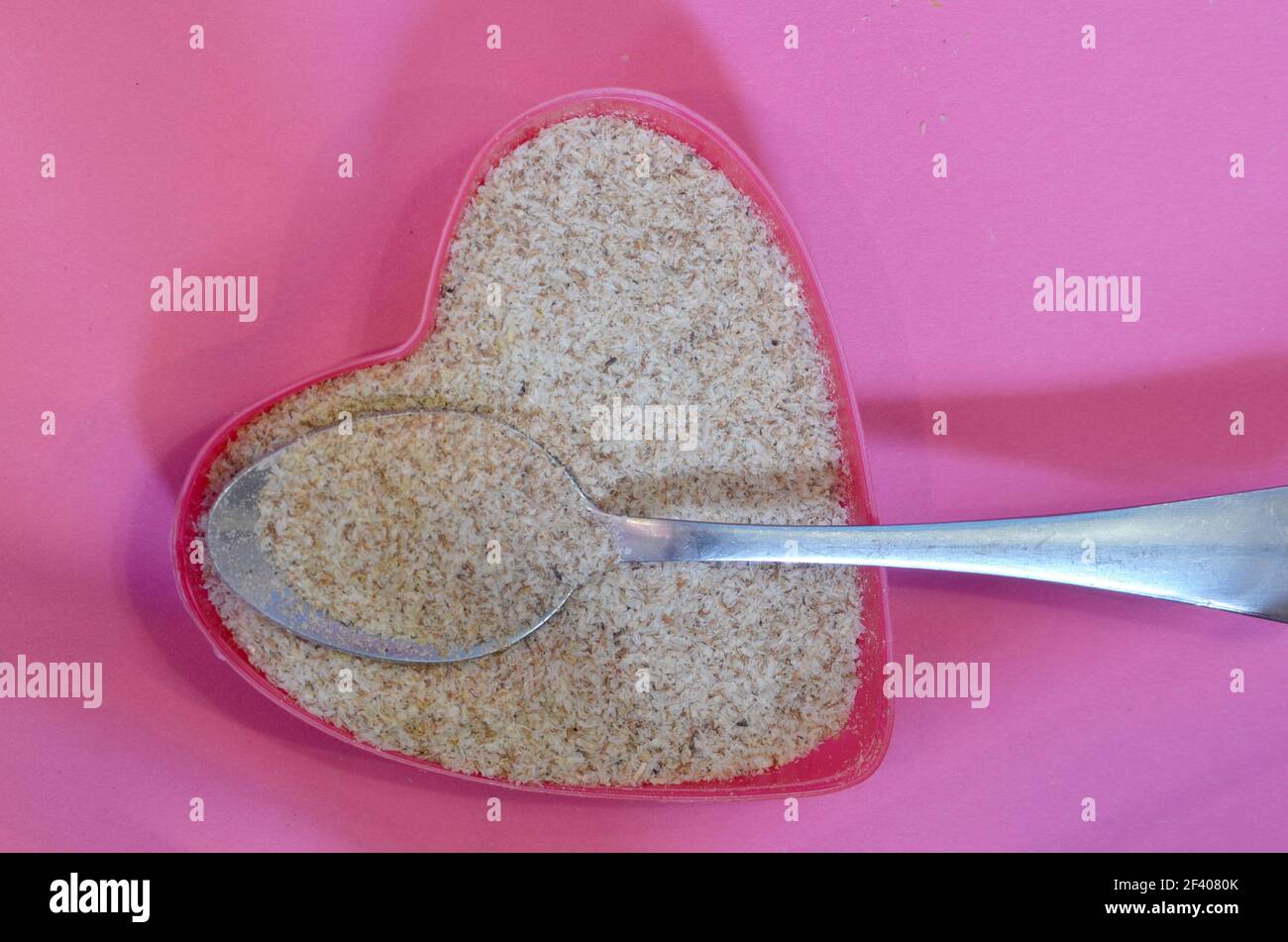 Psyllium a forma di cuore su sfondo rosa, vista dall'alto. Semi di psyllium di cibo eccellente, ingrediente di dieta del keto. Concetto di cibo sano Foto Stock