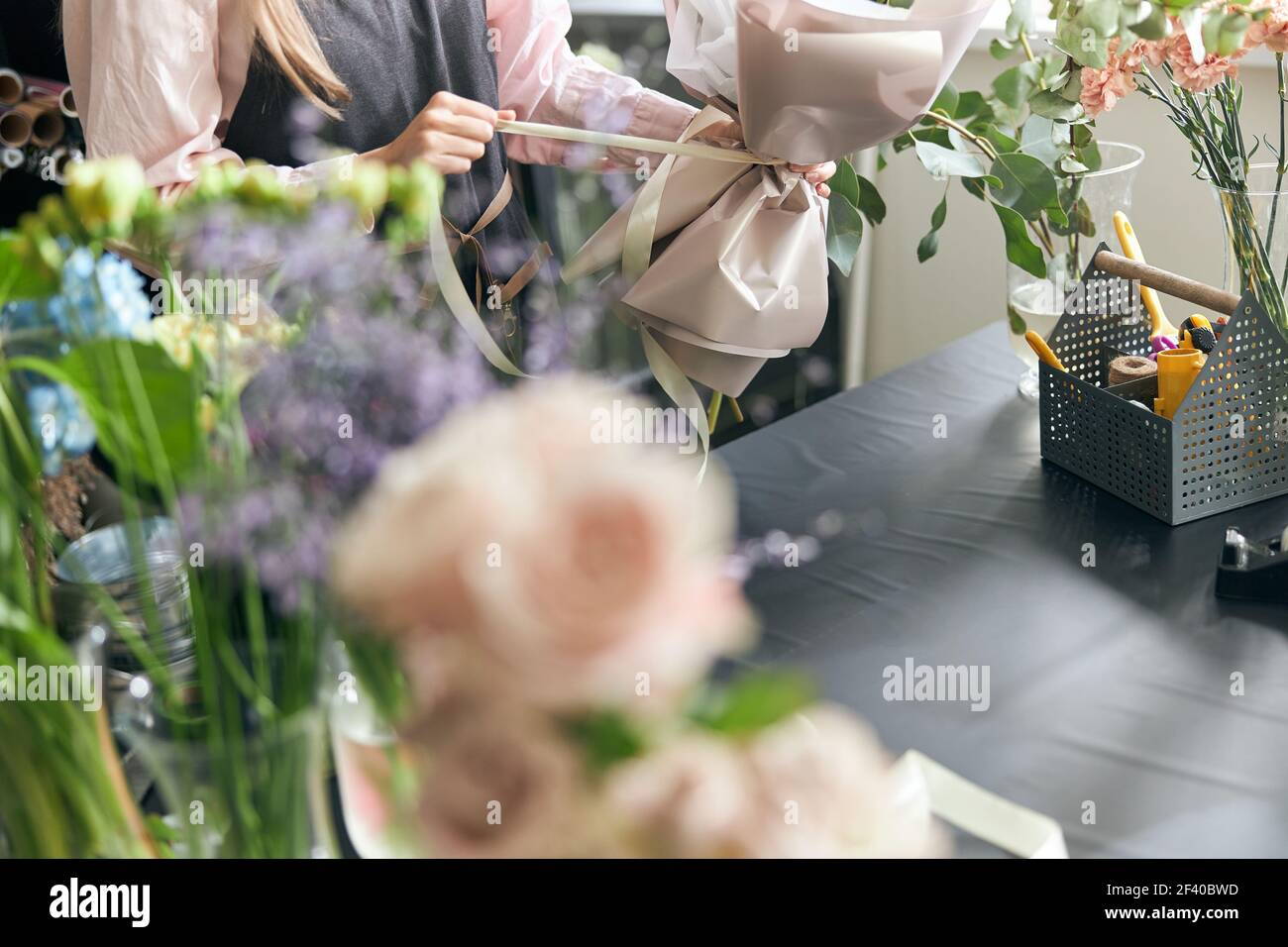 Fiorista che tiene il nastro decorativo mentre fa il bouquet in negozio di fiori. Bella composizione floreale. Dettaglio. Primo piano Foto Stock