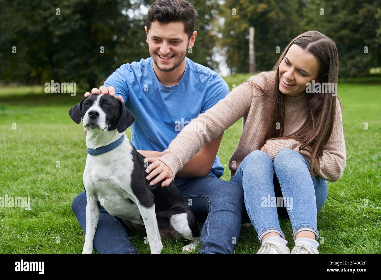 Giovane coppia seduta con cane animale domestico su erba nel parcheggio Foto Stock