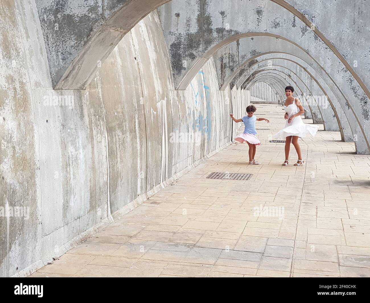 Funny madre e figlia ballare sotto le arcate del porto di Malaga in Andalusia, Spagna. Femmine indossando vestiti. Foto Stock