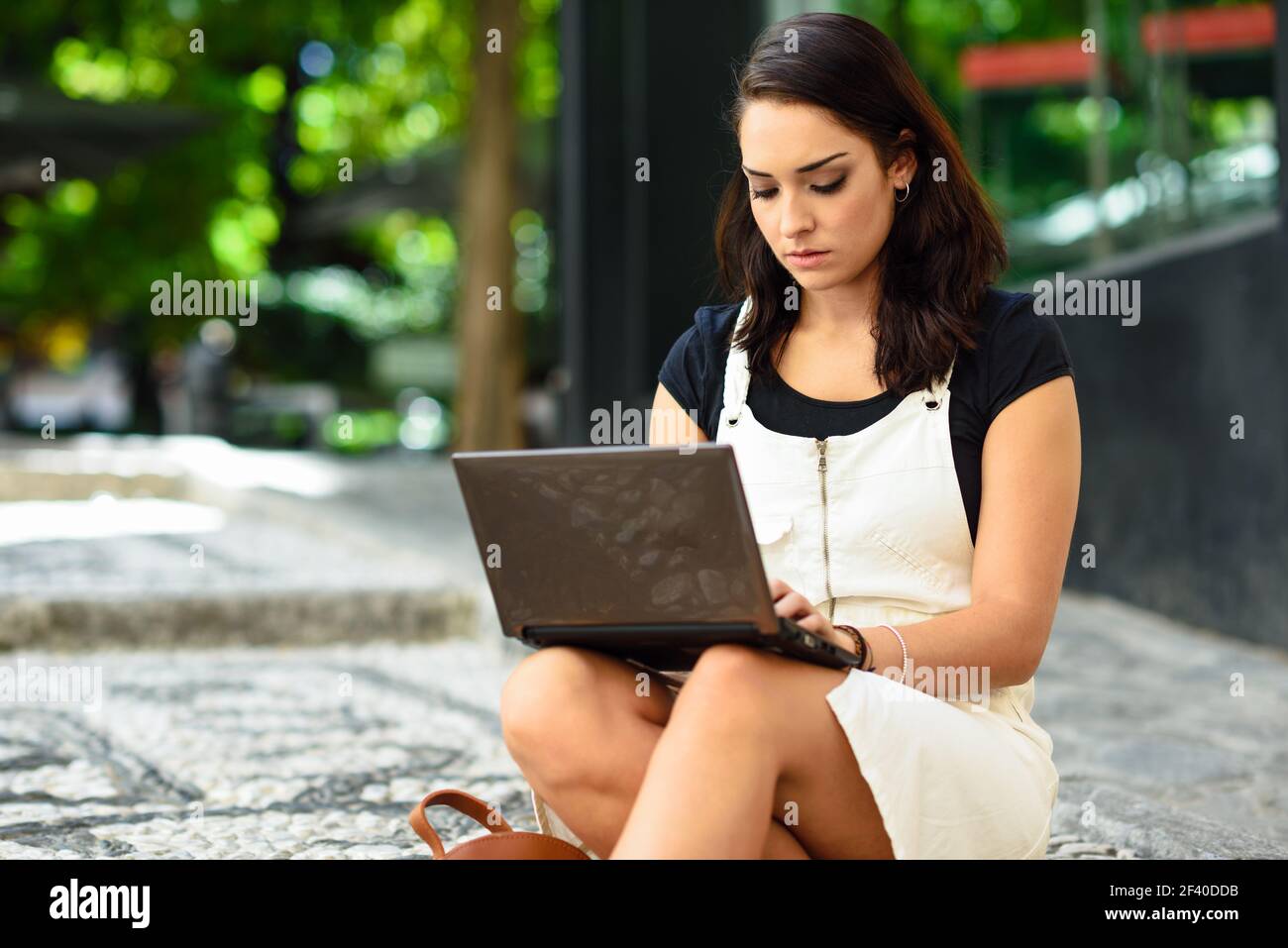 Bella giovane donna utilizzando computer portatile seduti sulle fasi di URBAN. Imprenditrice di indossare abiti casual per lavorare in esterno. Il concetto di stile di vita. Foto Stock