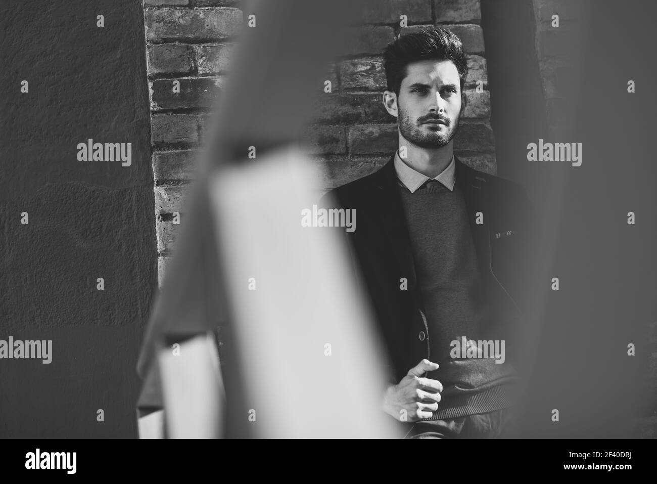 Uomo attraente per la strada che indossa un abito inglese elegante. Uomo d'affari giovane con acconciatura moderna in background urbano. Fotografia in bianco e nero. Foto Stock