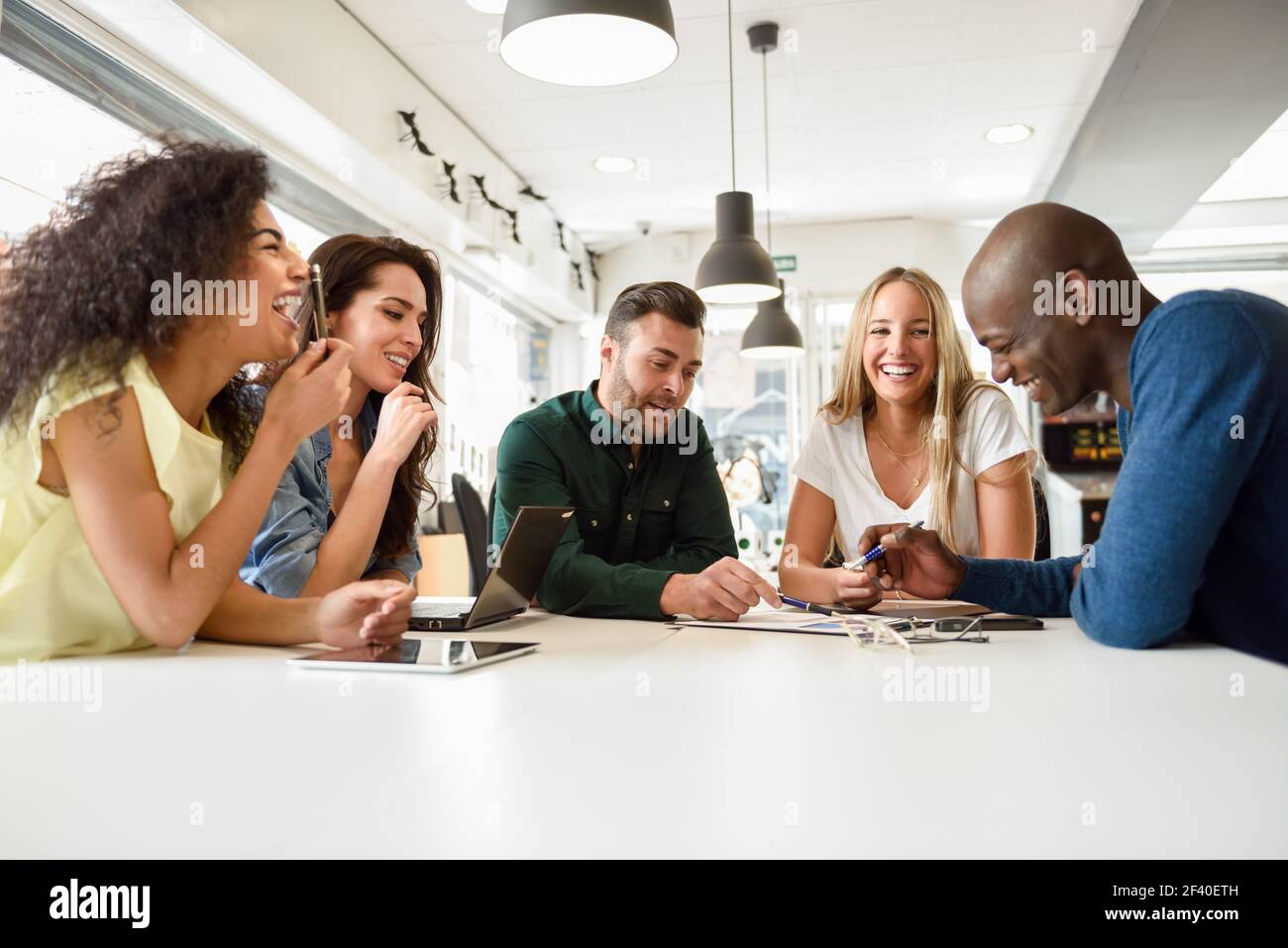 Cinque giovani che studiano con computer portatili e i computer tablet sulla scrivania bianca. Belle ragazze e ragazzi che lavorano insieme di indossare un abbigliamento informale. Multi-etnico gruppo sorridente. Foto Stock