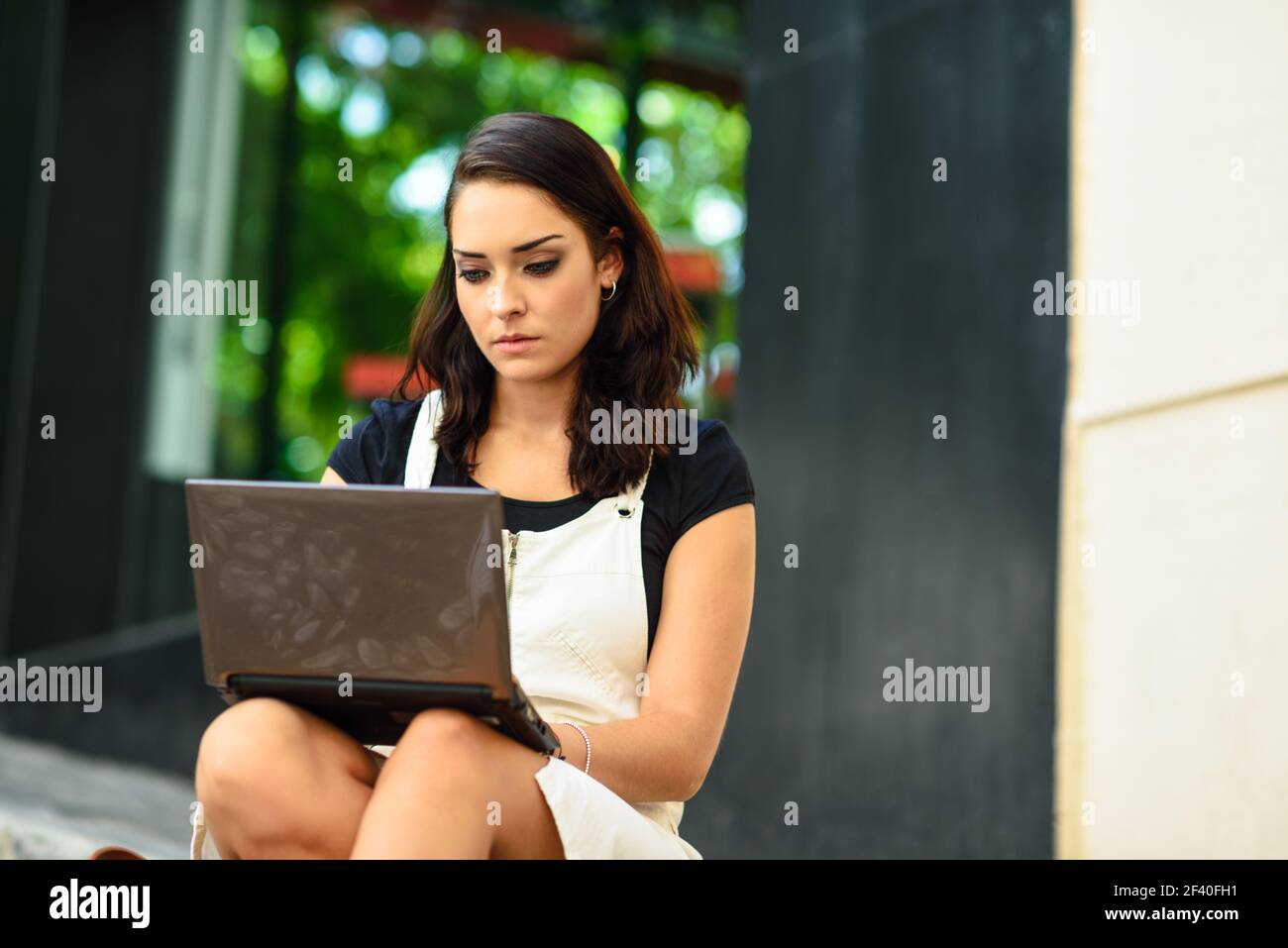 Bella giovane donna utilizzando computer portatile seduti sulle fasi di URBAN. Imprenditrice di indossare abiti casual per lavorare in esterno. Il concetto di stile di vita. Foto Stock