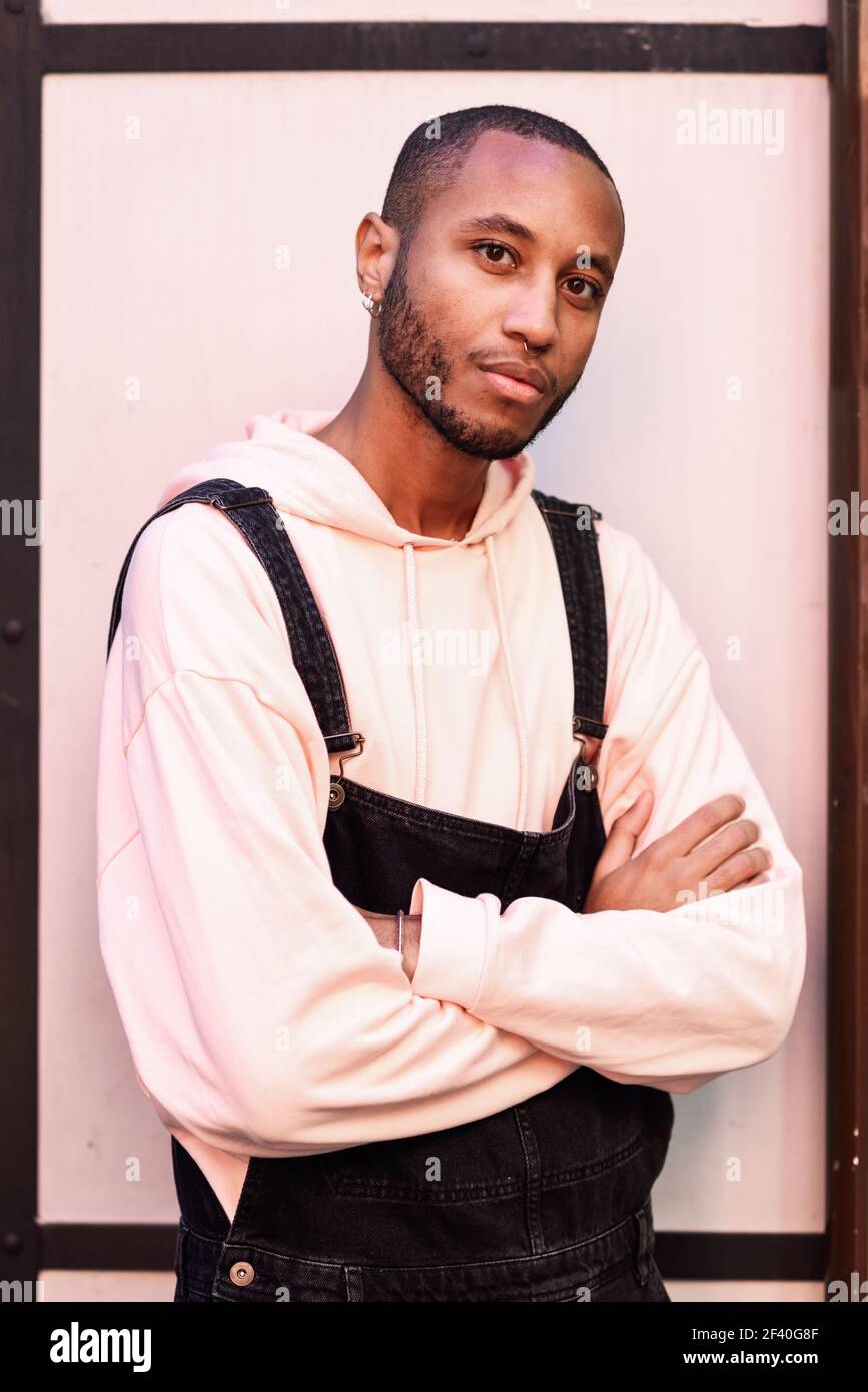 Uomo nero indossando abiti casual contro un rosso di fondo urbano. Ragazzo africano con bib pants all'aperto Foto Stock