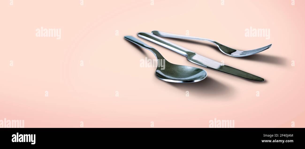 Cucchiaio forchetta e coltello isolati su sfondo salmone con copia spazio Foto Stock