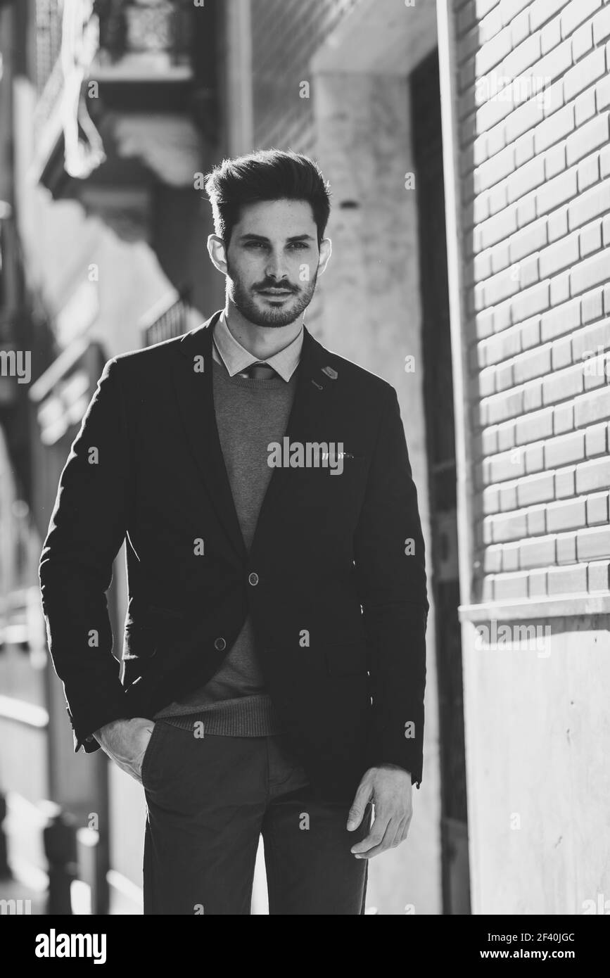 Uomo attraente per la strada che indossa un abito inglese elegante. Uomo d'affari giovane con acconciatura moderna in background urbano. Fotografia in bianco e nero. Uomo attraente che indossa un abito inglese elegante in strada. Capelli moderni. Foto Stock