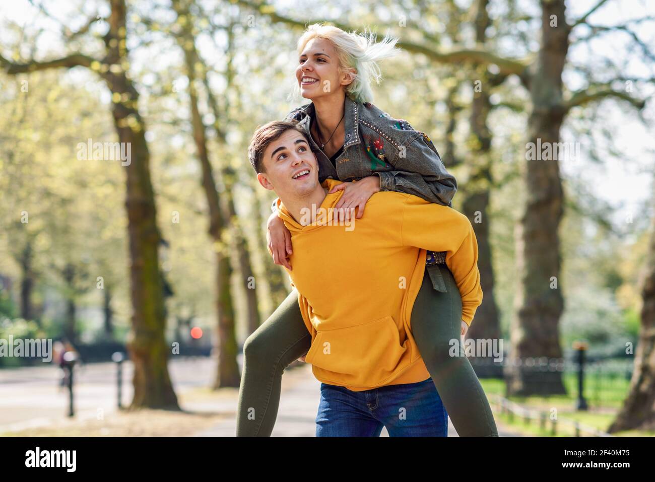 Coppia divertente in un parco urbano. Ragazzo che porta la sua fidanzata sul piggyback. Amore e tenerezza, datazione, romanticismo. Concetto di stile di vita. Coppia divertente in un parco urbano. Ragazzo che porta la sua fidanzata sul piggyback. Foto Stock