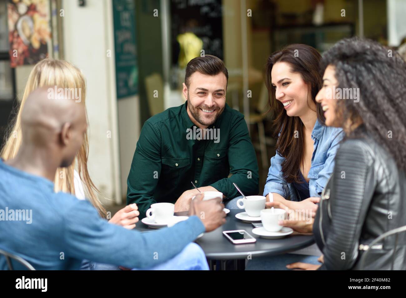 Gruppo multirazziale di cinque amici che hanno un caffè insieme. Tre donne e due uomini al caffè, parlando, ridendo e godendo il loro tempo. Stili di vita e concetti di amicizia con modelli di persone reali. Gruppo multirazziale di cinque amici che hanno un caffè insieme Foto Stock