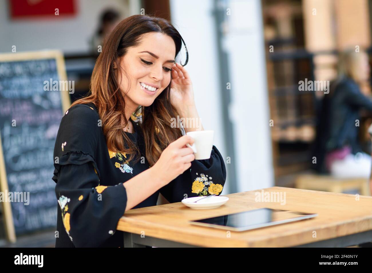 Donna di mezza età che beve caffè in un bar caffetteria urbano. Giovane donna seduta al tavolo in una terrazza esterna. Ragazza con la california mette in evidenza la acconciatura.. Donna di mezza età che beve caffè in un bar caffetteria urbano. Foto Stock