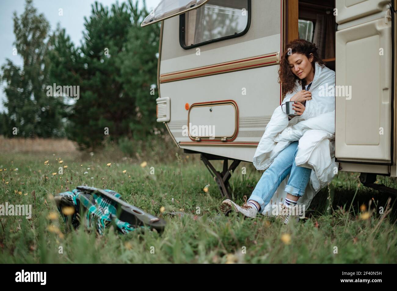 Ragazza seduta sulla scala del camper con una tazza dentro le sue mani avvolte in una coperta Foto Stock