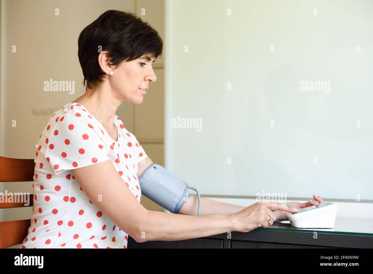 Donna di mezza età che misura la propria pressione sanguigna con un dispositivo elettronico per la misurazione della pressione sanguigna a casa. Donna che misura la propria pressione sanguigna a casa. Foto Stock
