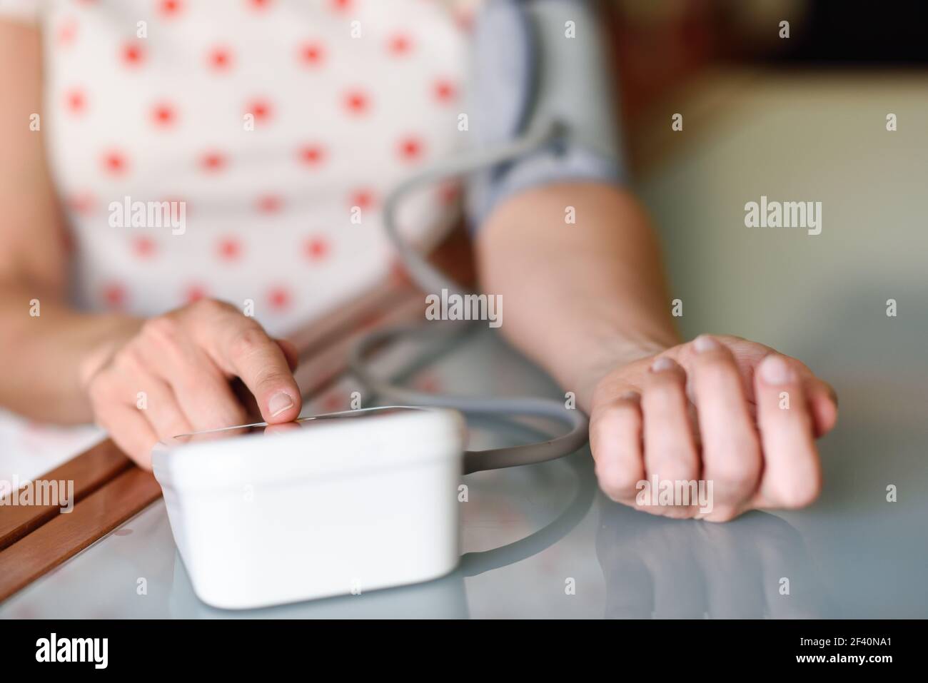 Donna di mezza età che misura la propria pressione sanguigna con un dispositivo elettronico per la misurazione della pressione sanguigna a casa. Donna che misura la propria pressione sanguigna a casa. Foto Stock