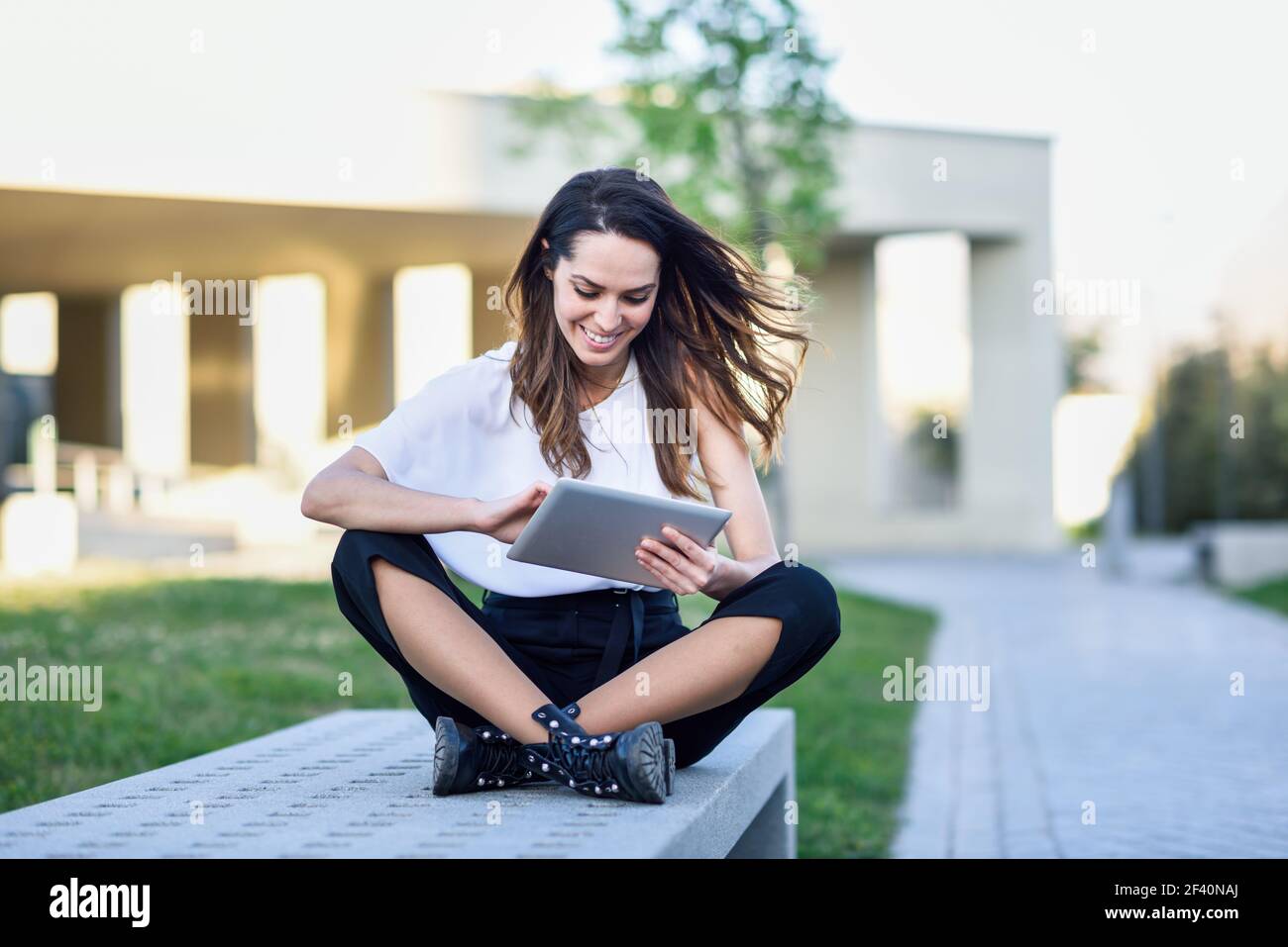 Giovane donna che usa un tablet digitale seduto all'aperto in ambiente urbano. Donna di mezza età che utilizza un tablet digitale seduto all'aperto in ambiente urbano. Foto Stock