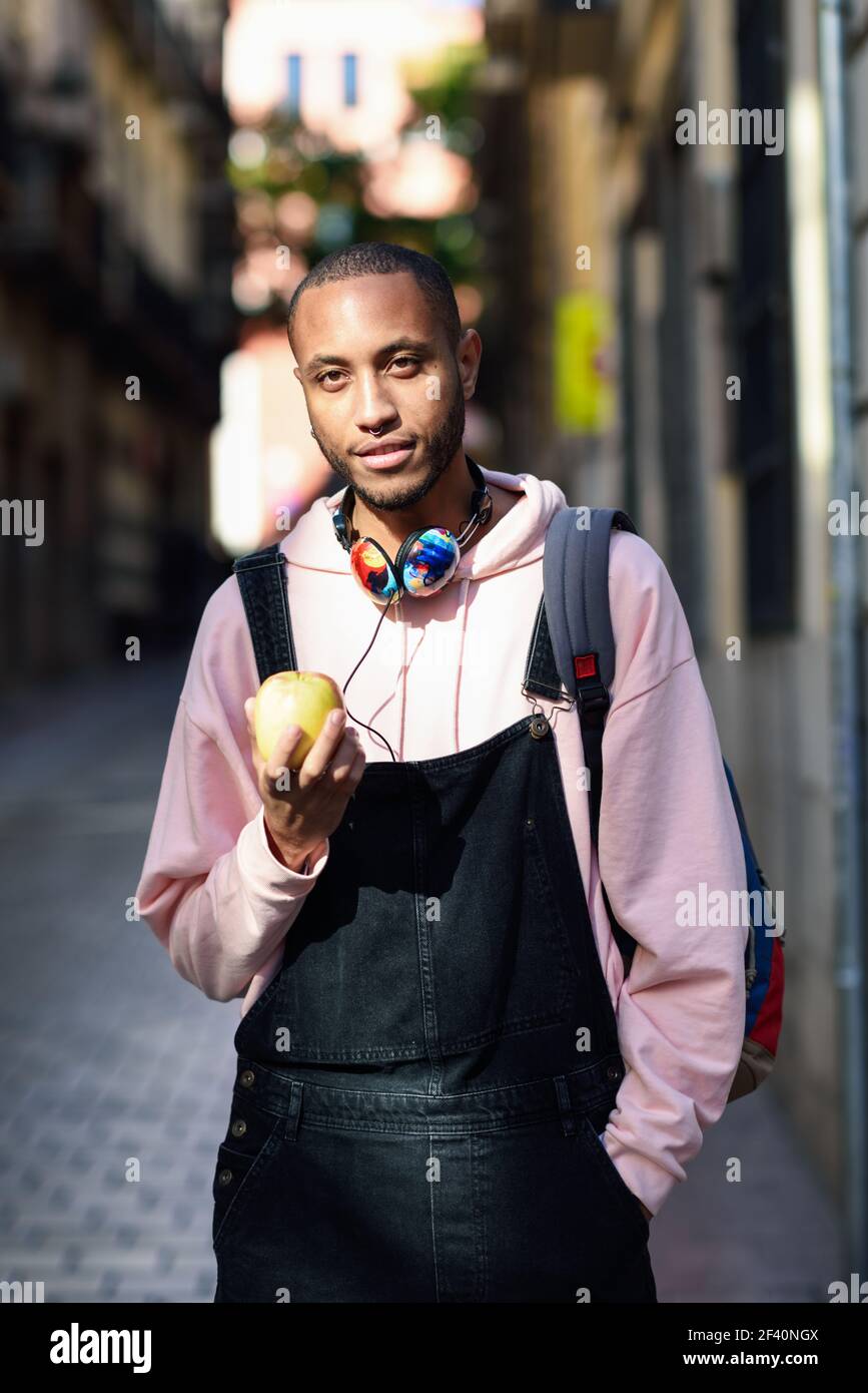 Giovane uomo nero che mangia una mela che cammina per la strada. Concetto di stile di vita.. Giovane uomo nero che mangia una mela che cammina per la strada. Foto Stock