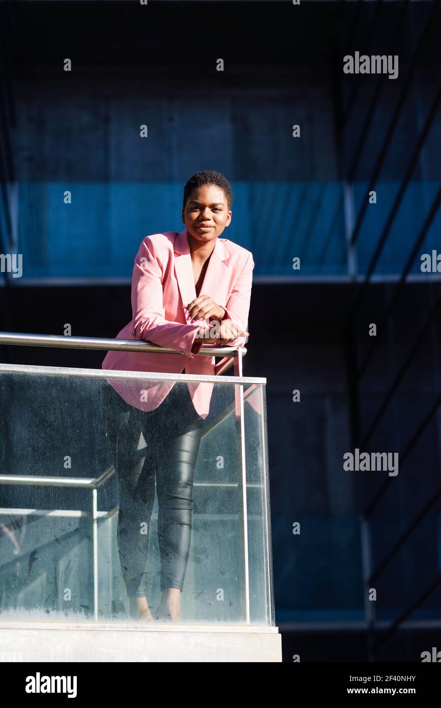 Donna d'affari nera felice in piedi vicino alla costruzione dell'ufficio di affari. Donna afroamericana con giacca rosa. Donna d'affari nera felice in piedi vicino alla costruzione dell'ufficio di affari. Foto Stock