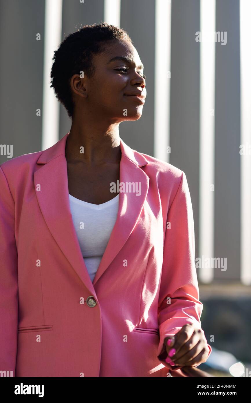 Donna d'affari nera in piedi vicino alla costruzione dell'ufficio di affari. Donna afroamericana con giacca rosa. Donna d'affari nera in piedi vicino alla costruzione dell'ufficio di affari. Foto Stock