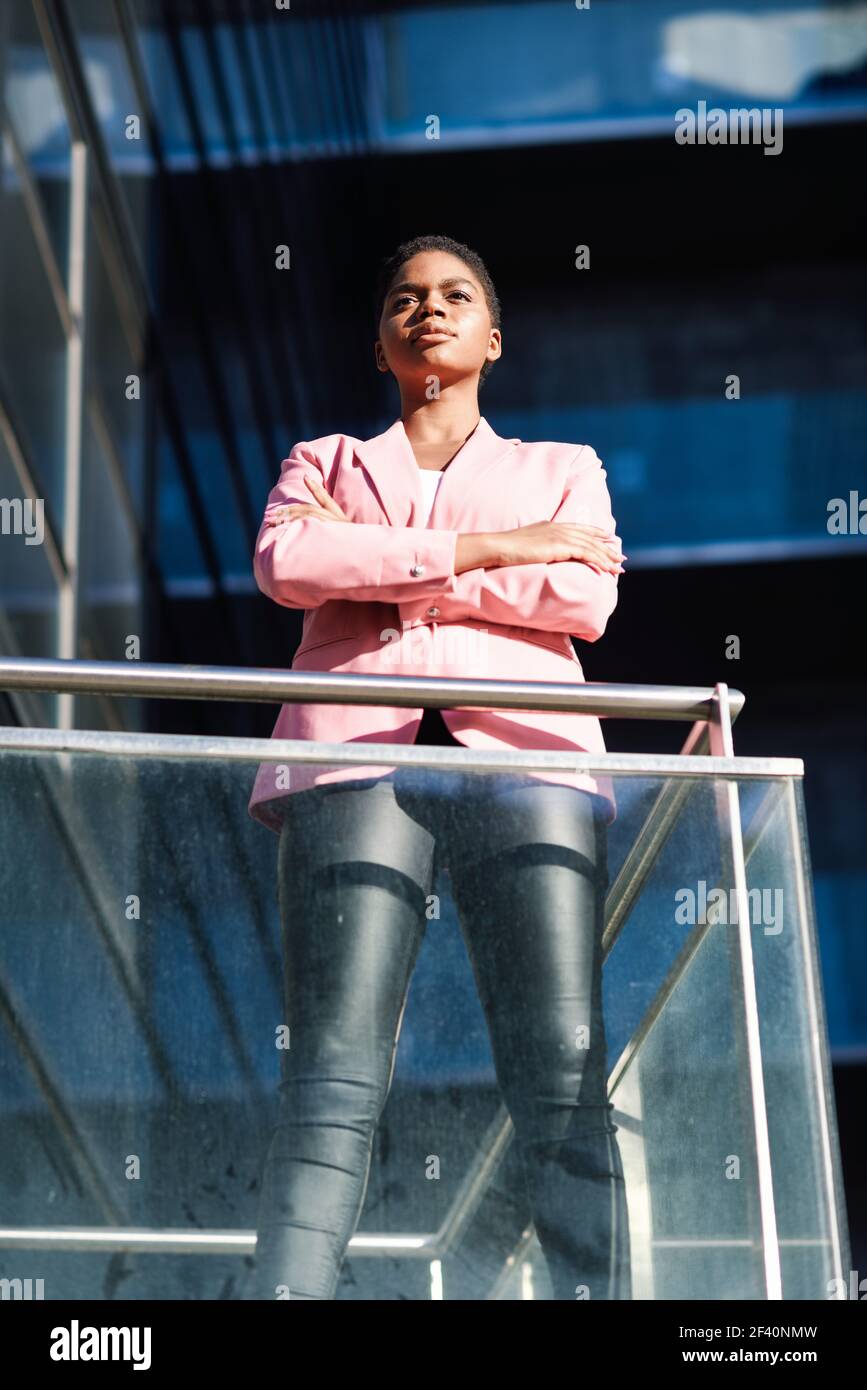 Donna d'affari nera in piedi vicino alla costruzione dell'ufficio di affari. Donna afroamericana con giacca rosa. Donna d'affari africana in piedi vicino alla costruzione dell'ufficio di affari. Foto Stock