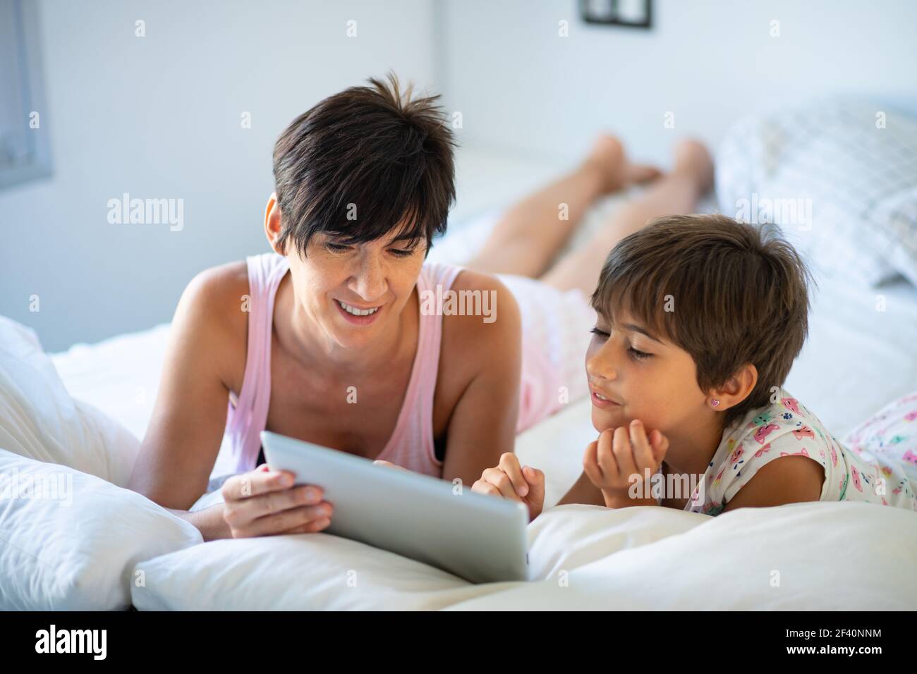 Divertente mamma e bella bambina si divertono sul letto. Madre di mezza età con la figlia di otto anni che usa un tablet digitale in camera da letto. Madre di mezza età con la figlia di otto anni che usa un tablet digitale in camera da letto. Foto Stock