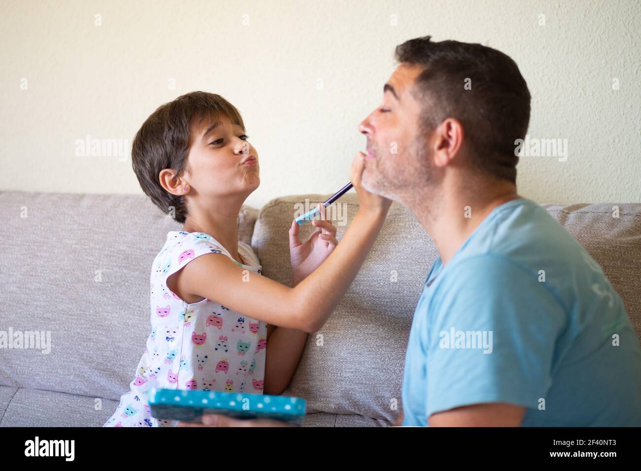 Piccola figlia carina che fa il make-up a suo padre. Papà trascorrere del tempo libero con sua figlia. Concetto di mascolinità alternativo.. Piccola figlia carina che fa il make-up a suo padre Foto Stock