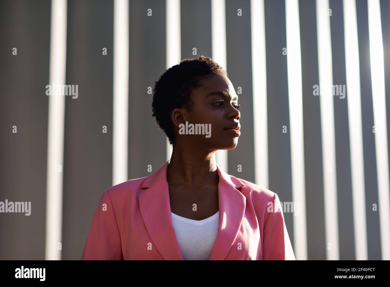 Donna d'affari nera sorridente in piedi vicino alla costruzione dell'ufficio di affari. Donna afroamericana con giacca rosa. Donna d'affari nera sorridente in piedi vicino alla costruzione dell'ufficio di affari Foto Stock