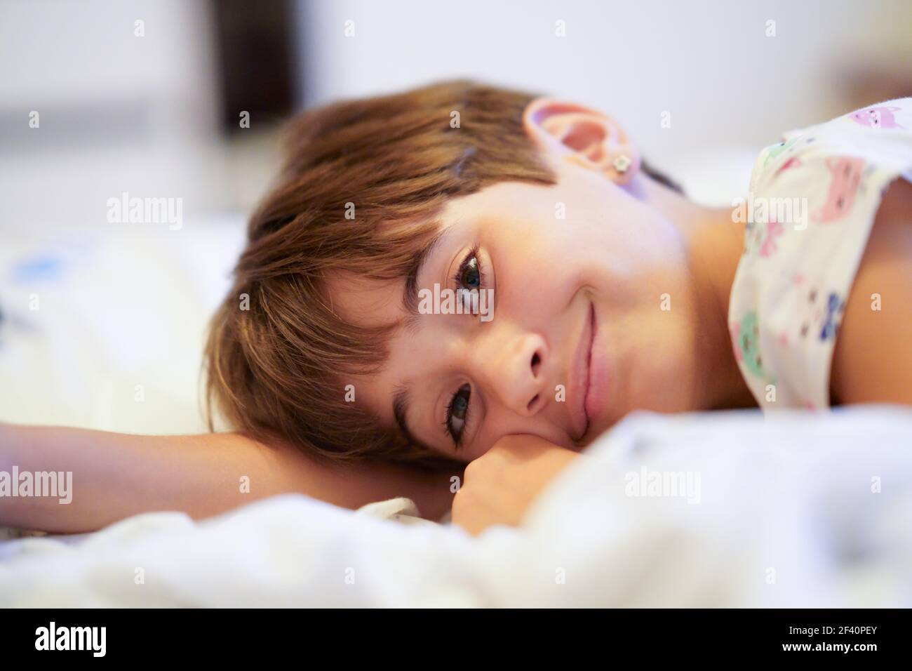 Felice bambina, di otto anni, sdraiata sul suo letto a casa, sorridente alla macchina fotografica. Bambina, di otto anni, sdraiata sul suo letto Foto Stock