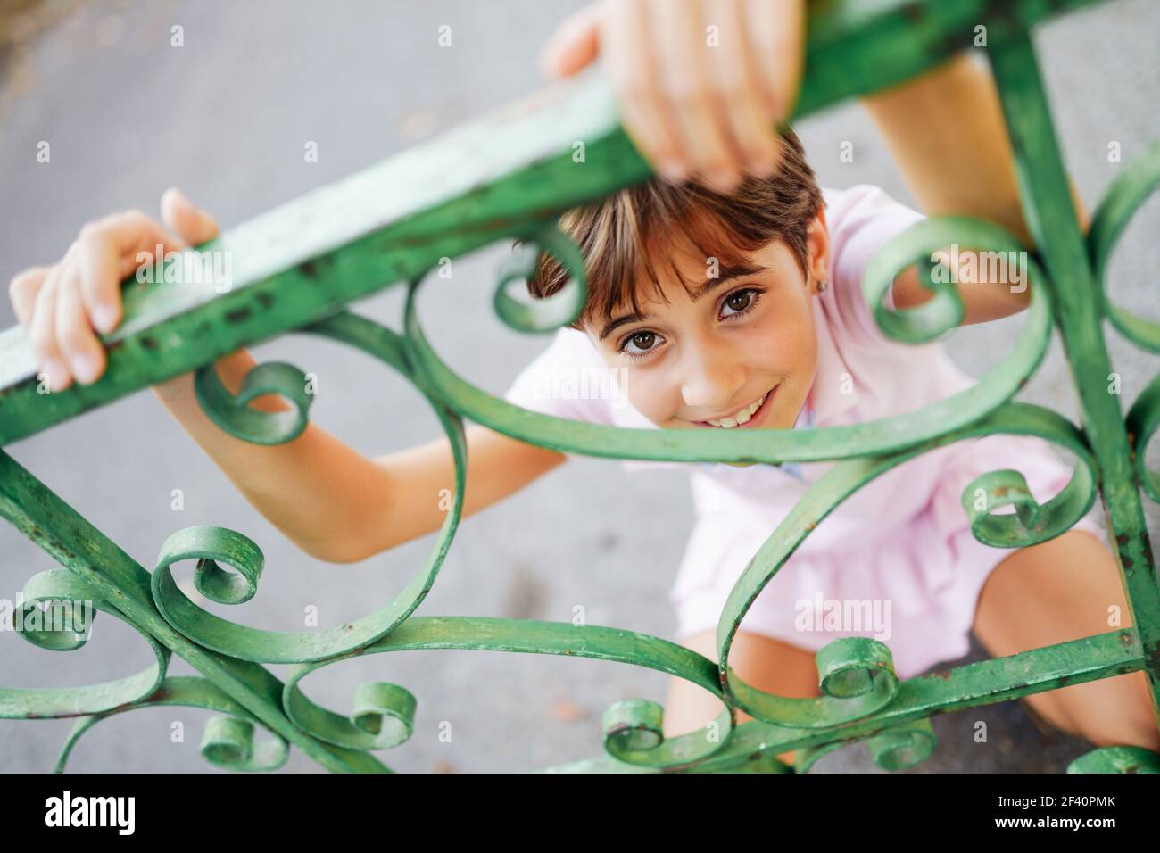Bambina, con capelli corti, che gioca con una recinzione in ferro battuto. Bambina, otto anni, che si diverte in un parco urbano. Foto Stock