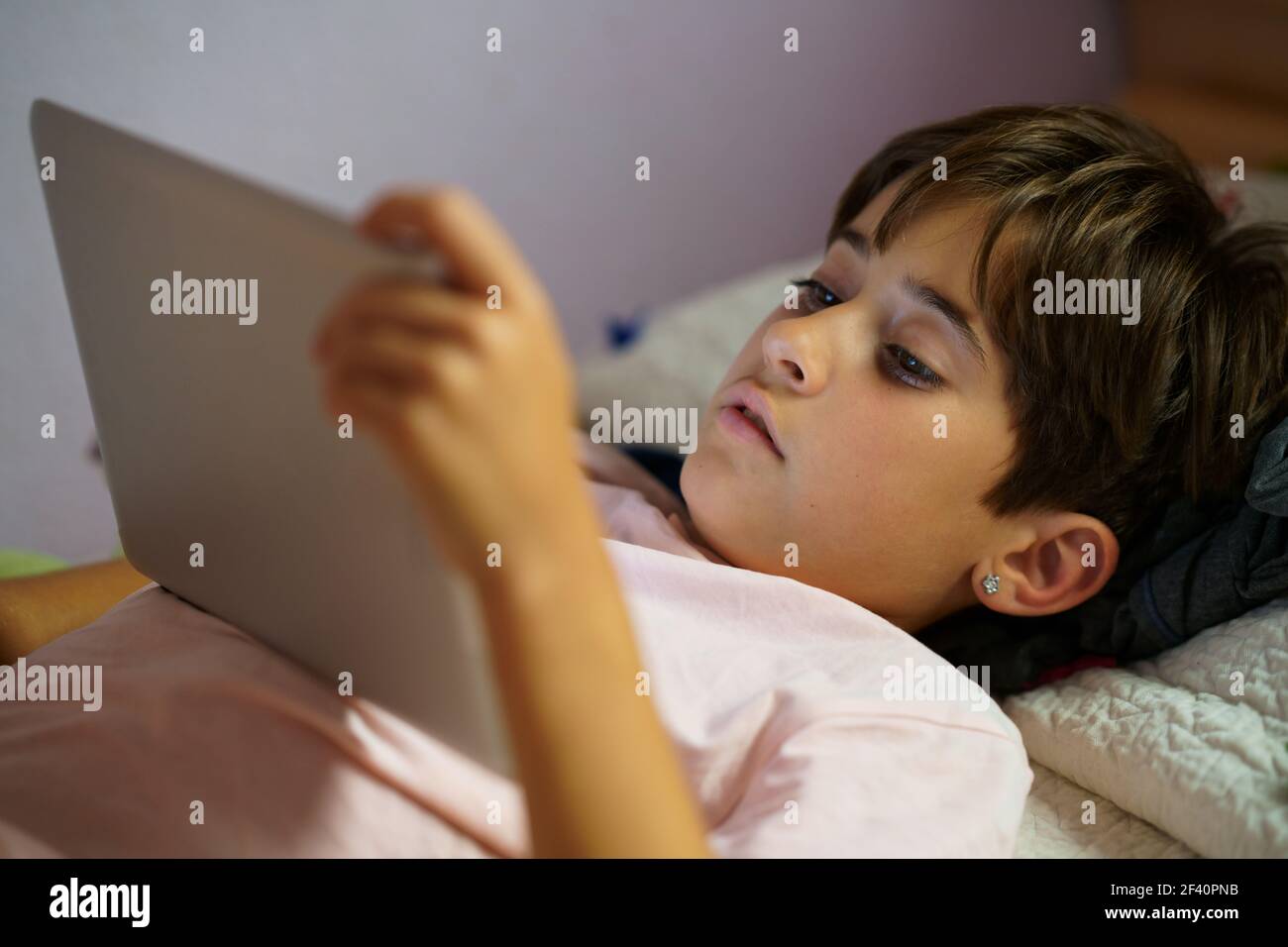 Ragazza carina, di otto anni, che usa un computer tablet in camera da letto. Ragazza con capelli corti.. Ragazza carina che usa un computer tablet nella sua camera da letto Foto Stock