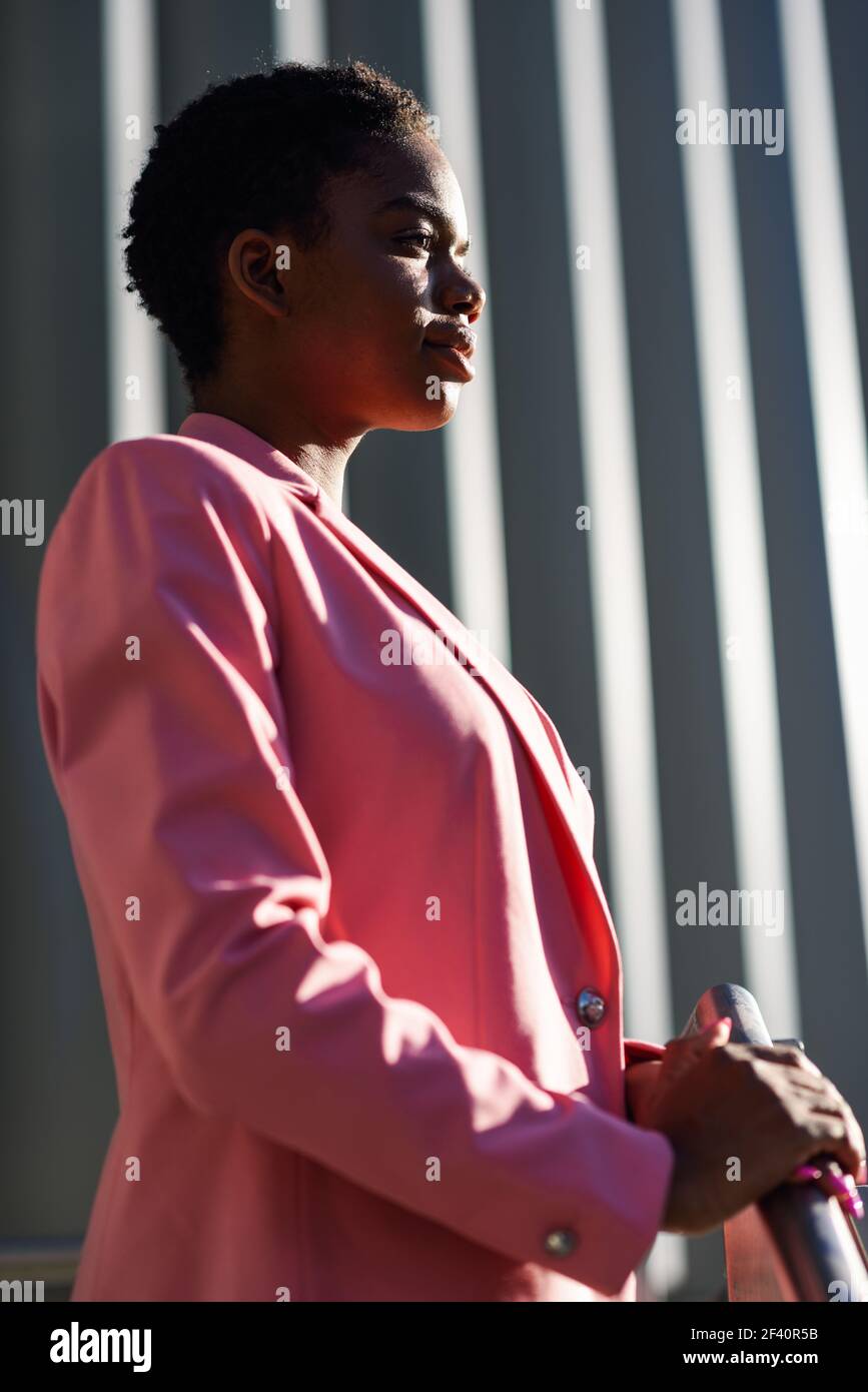 Donna d'affari nera in piedi vicino alla costruzione dell'ufficio di affari. Donna afroamericana con giacca rosa. Donna d'affari nera in piedi vicino alla costruzione dell'ufficio di affari. Foto Stock
