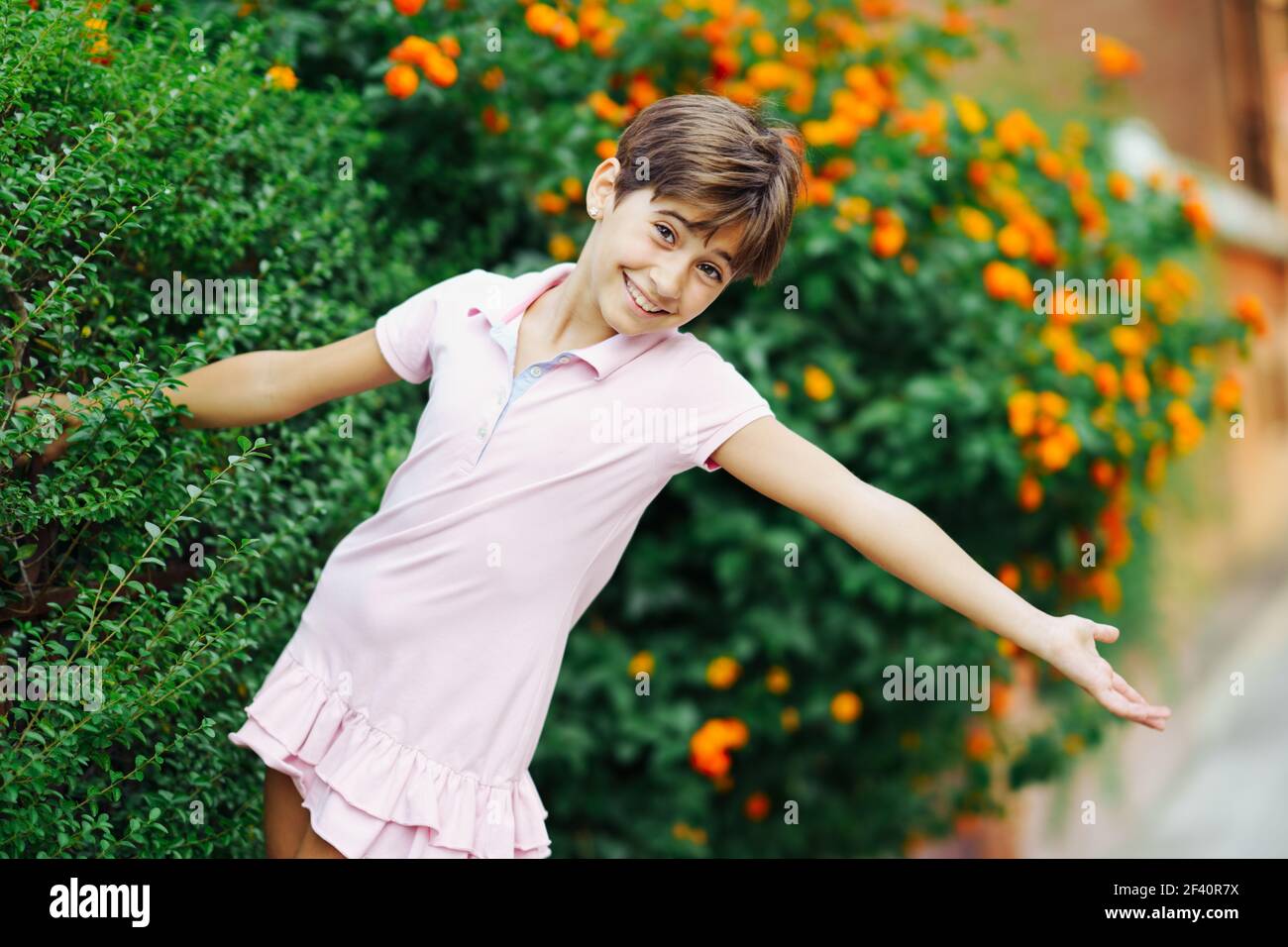 Bambina con capelli molto corti, divertirsi in un parco urbano con vestito rosa. Bambina, otto anni, che si diverte in un parco urbano. Foto Stock